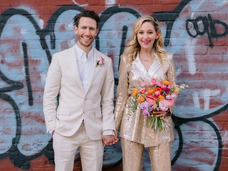 wedding pictures of jen glantz and her husband in front of brick, graffitied wall