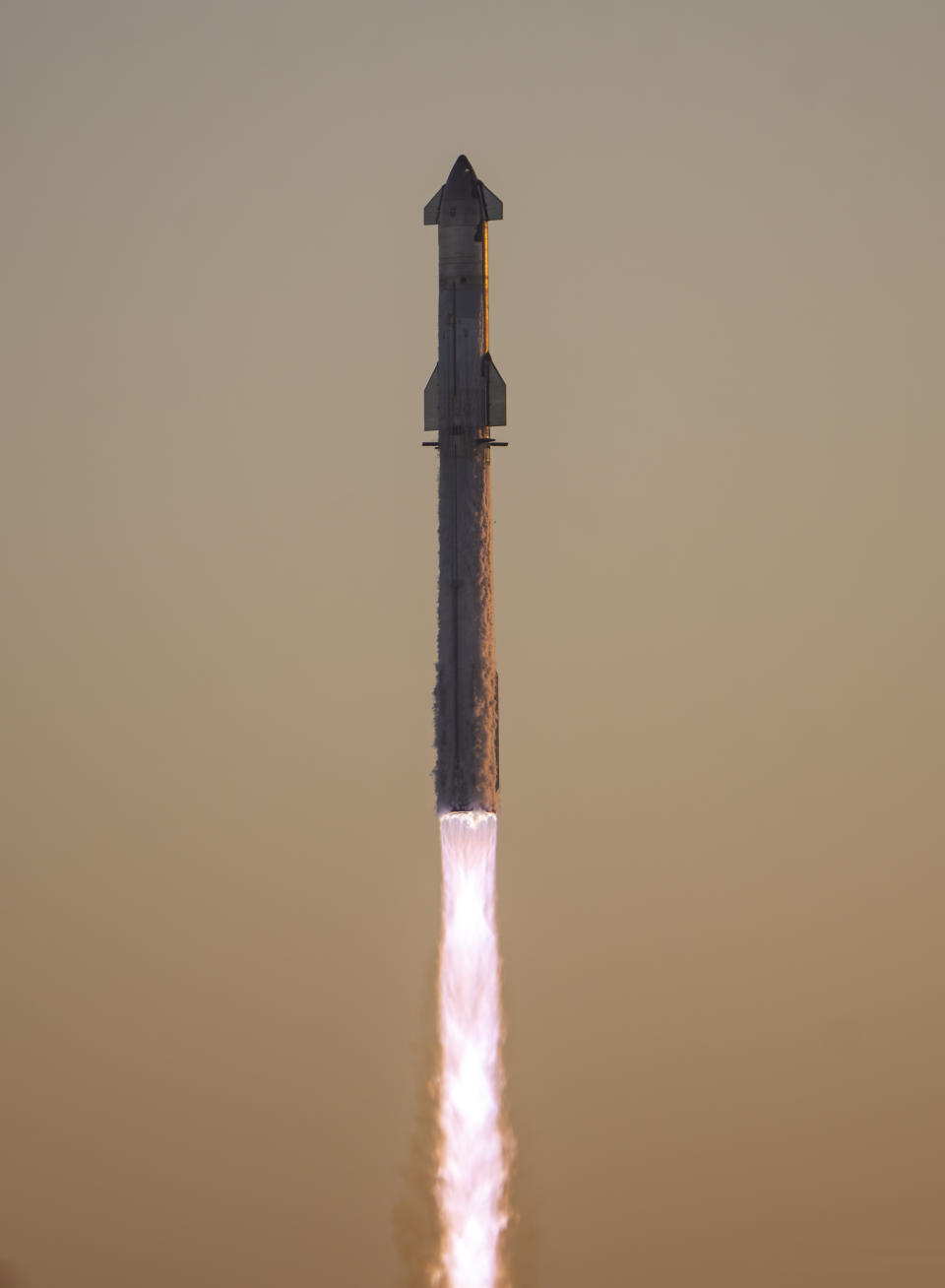 A giant rocket lifts off at sunrise with its fins and booster in silhouette