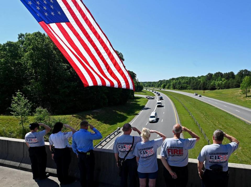 Members of the Lucia-Riverbend Fire Dept. and Gaston Emergency Medical Services stand at attention as the hearse carrying the body of slain officer Alden Elliott travels along N.C. 16 on Thursday, May 2, 2024. The procession traveled from Charlotte to Newton, NC. Elliott, a 14-year officer with the North Carolina Department of Adult Correction, died on Monday, April 29th, 2024 when serving a warrant in east Charlotte