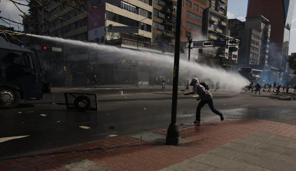 A masked anti-government protester throws a stone at a spraying water canon operated by Bolivarian National Police during clashes in Caracas, Venezuela, Saturday, March 22, 2014. Two more people were reported dead in Venezuela as a result of anti-government protests even as supporters and opponents of President Nicolas Maduro took to the streets on Saturday in new shows of force.(AP Photo/Fernando Llano)