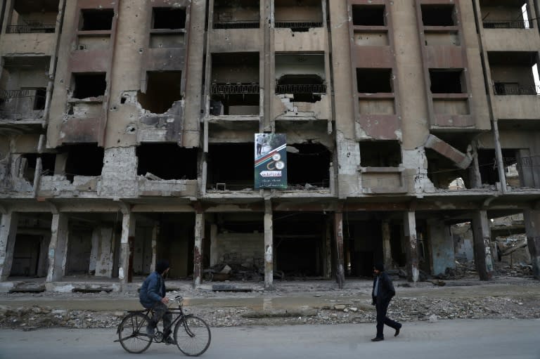 Syrians walk past a damaged building in the rebel-held town of Douma, on the eastern outskirts of the capital Damascus, on January 20, 2017