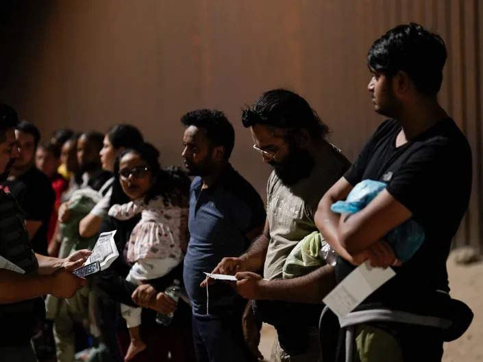 Migrants wait to be processed by Border Patrol agents near the end of a border wall Tuesday, Aug. 23, 2022, near Yuma, Arizona.