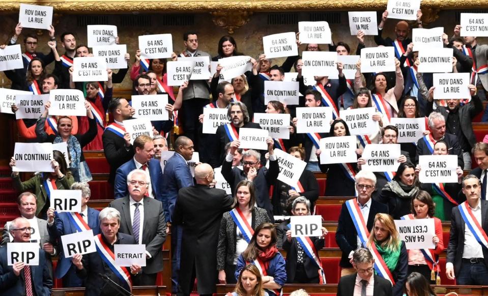 Opposition MPs hold signs reading ‘64 is a no’ and ‘See you in the streets’ after narrowly losing a no-confidence vote over pension reforms (AFP via Getty Images)