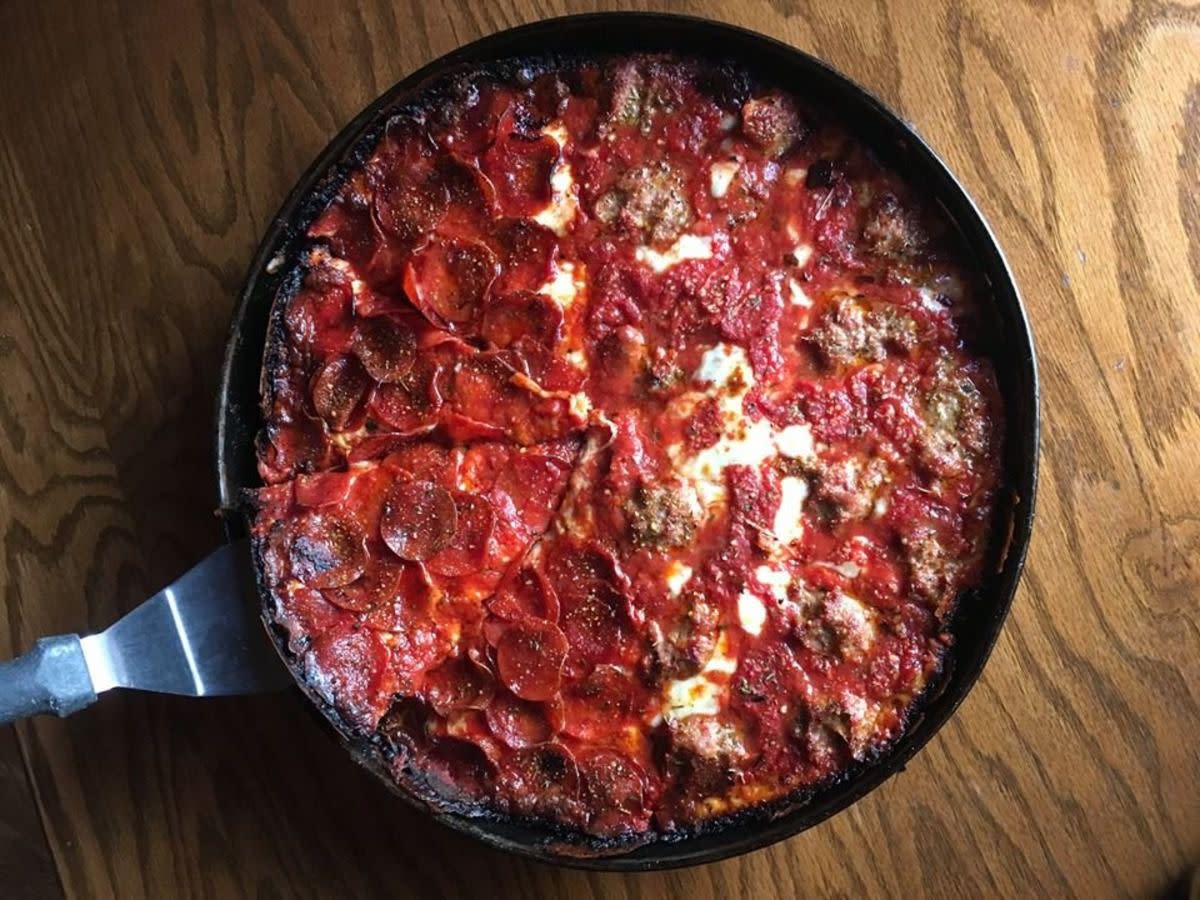 Top-view of half pepperoni, half sausage Chicago Pizza in oven tray with spatula under a piece, Pequod's Pizza, Chicago, on a wooden table