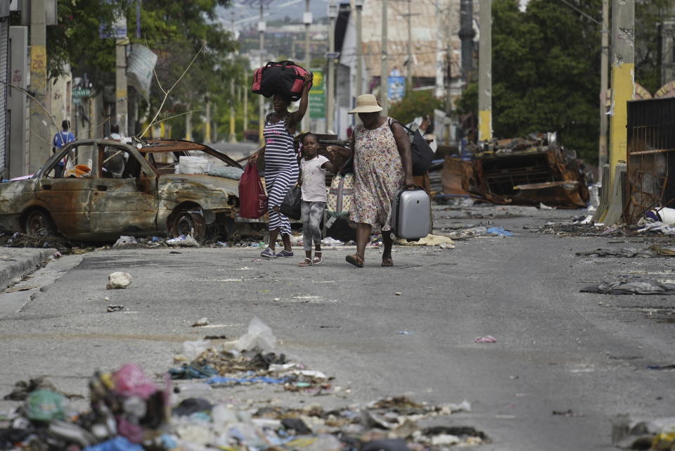 Residents walk past a burnt car blocking the street as they evacuate the Delmas 22 neighborhood to escape gang violence in Port-au-Prince, Haiti, Thursday, May 2, 2024. (AP Photo/Ramon Espinosa)