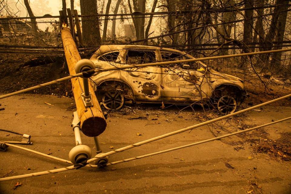 The charred remains of a vehicle is ensnared amid power lines near a fallen telephone pole on Pearson Road in Paradise in 2018, near where multiple people lost their lives in the Camp Fire according to the Butte County Sheriff’s Office.