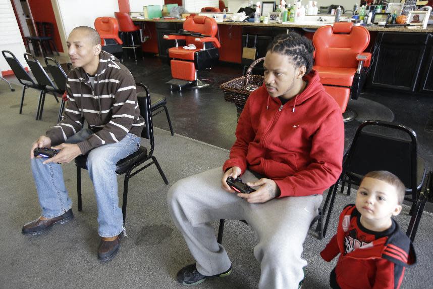 In this Tuesday, Jan. 28, 2014 photo, barbers Tarris Horton, left, and England Wesley play a video game while they wait for customers at Hair on the Floor Barbershop in Covington, Ky. Wesley says business at the barbershop, which depends heavily on walk-in clientele, has been down about 90 percent in the past several weeks. One-year-old Kannon Wesley watches at right. (AP Photo)