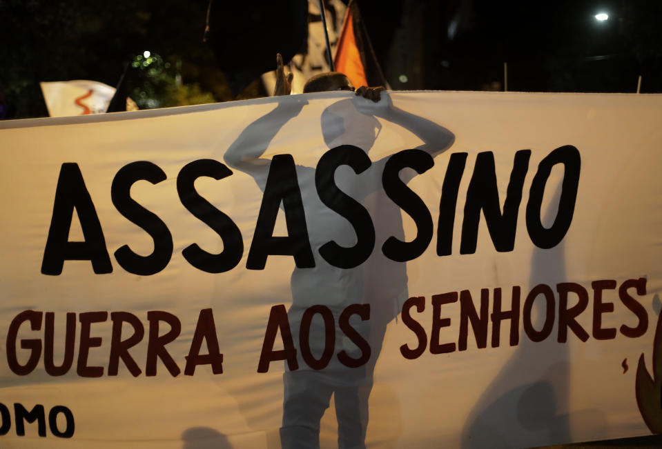 FILE - In this Tuesday, July 13, 2021 file photo, a demonstrator stands behind a banner that reads in Portuguese "Assassin," in reference to Brazilian President Jair Bolsonaro, during a protest calling for the resignation of Bolsonaro, who is fighting corruption charges in Senate hearings investigating the purchase of vaccines to fight the COVID-19 pandemic, in Rio de Janeiro , Brazil. The coronavirus pandemic has upended life around the globe, but it has hasn’t stopped the spread of authoritarianism and extremism. Some researchers believe it may even have accelerated it, but curbing individual freedoms and boosting the reach of the state. Since COVID-19 hit, Hungary has banned children from being told about homosexuality. China shut Hong Kong’s last pro-democracy newspaper. Brazil’s president has extolled dictatorship. Belarus has hijacked a passenger plane. A Cambodian human rights lawyer calls the pandemic “a dictator's dream opportunity.” But there are also resistance movements, as protesters from Hungary to Brazil take to the streets to defend democracy. (AP Photo/Bruna Prado, File)