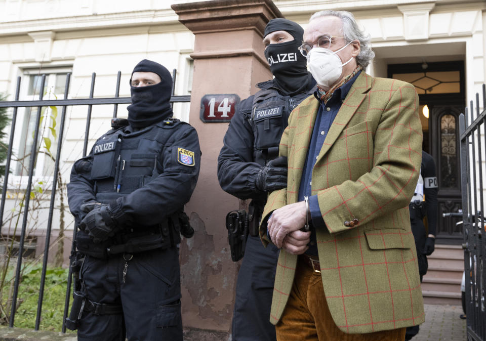 Masked police officers lead Heinrich XIII Prince Reuss, right, to a police vehicle during a raid against so-called 'Reich citizens' in Frankfurt, Germany, Wednesday, Dec. 7, 2022. Thousands of police carried out a series of raids across much of Germany on Wednesday against suspected far-right extremists who allegedly sought to overthrow the state by force. Federal prosecutors said some 3,000 officers conducted searches at 130 sites in 11 of Germany's 16 states against adherents of the so-called Reich Citizens movement. Some members of the grouping reject Germany's postwar constitution and have called for the overthrow of the government. (Boris Roessler/dpa via AP)