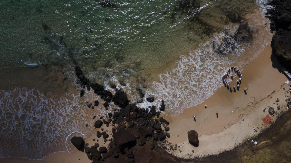 The family of Carolina Espinoza makes a circle around her and her newborn Himene as part of a a ceremony presenting her daughter to the sea, on Ovahe Beach on Rapa Nui, or Easter Island, Chile, Saturday, Nov. 26, 2022. (AP Photo/Esteban Felix)