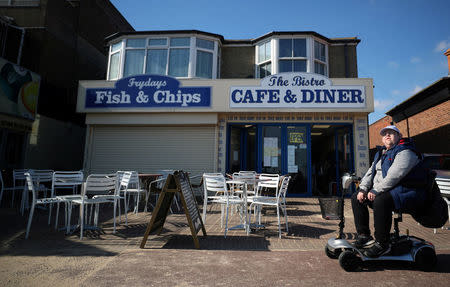 A man sits outside a cafe on the seafront in Great Yarmouth, Britain, March 21, 2018. REUTERS/Hannah McKay/Files