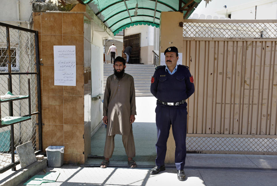 A Pakistani police officer stands guard with a worker of a religious group at the entrance to a mosque in Islamabad, Pakistan, Wednesday, March 6, 2019. Pakistan on Wednesday continued a crackdown on seminaries, mosques and hospitals belonging to outlawed groups, saying the actions were part of the government efforts aimed at fighting terrorism, extremism and militancy. (AP Photo/Anjum Naveed)