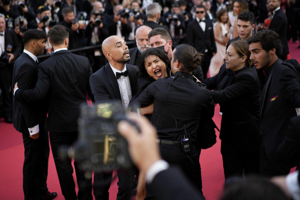 Una manifestante con pintura corporal que dice "Dejen de violarnos" y los colores de la bandera de Ucrania es retirada de la alfombra roja durante el estreno de la película "Three Thousand Years of Longing" en la 75ta edición del Festival de Cine de Cannes, en el sur de Francia, el viernes 20 de mayo de 2022. (Foto AP/Daniel Cole)