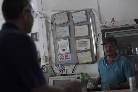 Roberto Torres (R) attends to a client next to government-issued licences and permits at his bar in San Juan, Puerto Rico, November 4, 2016. REUTERS/Alvin Baez