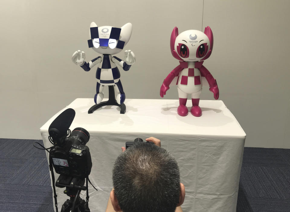 In this Thursday, July 18, 2019, photo, a journalist takes a photo of robots of mascots of Olympics "Miraitowa," left, and Paralympics "Someity" shown at Toyota Motor Corp. headquarters in Tokyo. The mascot robots’ eyes change to the images of stars and hearts. The Japanese automaker Toyota, a major Olympic sponsor, is readying various robots for next year’s Tokyo Olympics. (AP Photo/Yuri Kageyama)
