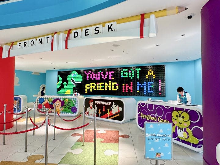 The Front Desk of Tokyo's Toy Story Hotel is marked with Scrabble pieces and a sign that resembles a classic Lite-Brite toy. In this image, it reads "You've got a friend in me," and shows a green and yellow dinosaur.