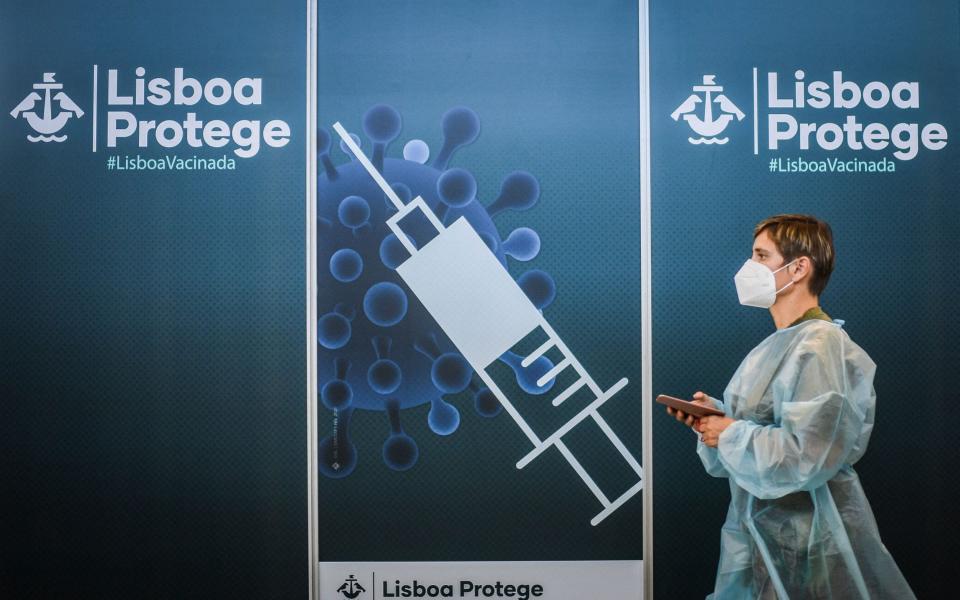 A healthworker walks by a poster at a Covid-19 vaccination center in Lisbon on July 2, 2021. - Nearly half of Portugal's population will be placed under night-time curfews again from Friday as the government seeks to rein in a resurgence in coronavirus infections, primarily due to the more contagious Delta variant.  - AFP