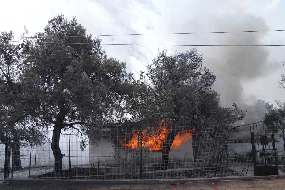 Flames and smoke comes out from the window of a house during a wildfire in Thea area some 60 kilometers (37 miles) northwest of Athens, Greece, Thursday, Aug. 19, 2021. A major wildfire northwest of the Greek capital devoured large tracts of pine forest for a third day and threatened a large village as hundreds of firefighters, assisted by water-dropping planes and helicopters, battled the flames Wednesday. (AP Photo/Thanassis Stavrakis)