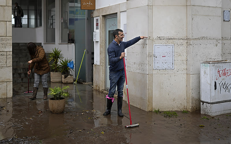 A man sweeping water from a building shows passersby the height that the water reached when the street was flooded overnight in Alges, just outside Lisbon, Portugal, on Dec. 13. An Atlantic storm slammed into the Iberian Peninsula, leaving behind a trail of destruction Tuesday, especially in the Portuguese capital of Lisbon, before moving eastward into Spain. <em>Associated Press/Armando Franca</em>