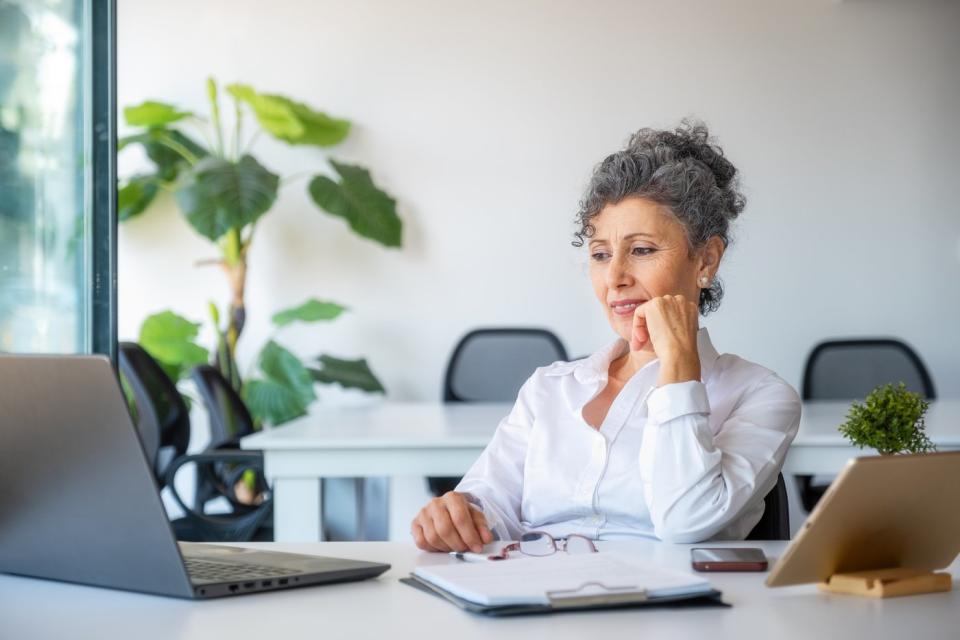 A senior woman sitting at a table looking at a laptop.