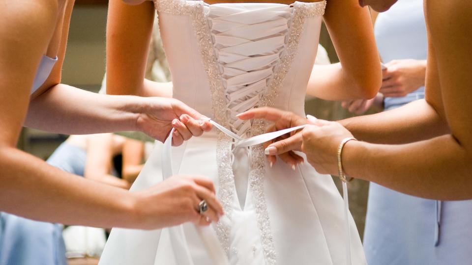 Back of bride's dress with bridesmaids in blue helping her into it. 