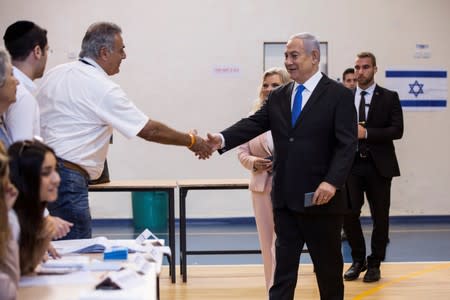 Israeli Prime Minister Benjamin Netanyahu greets a man as he arrives with his wife Sara to vote during Israel's parliamentary election at a polling station in Jerusalem