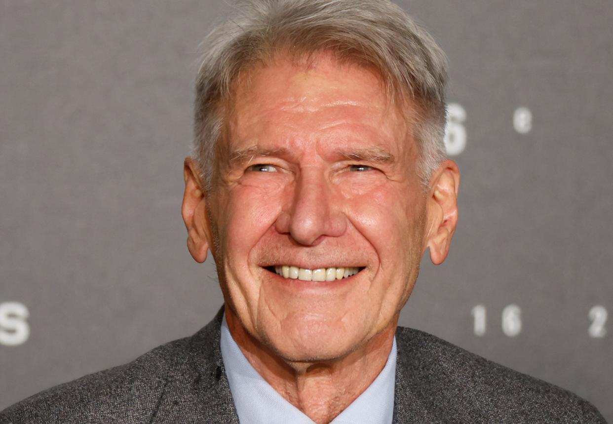 A close-up photo of Harrison Ford's face as he smiles in front of a grey backdrop at the Cannes Film Festival.