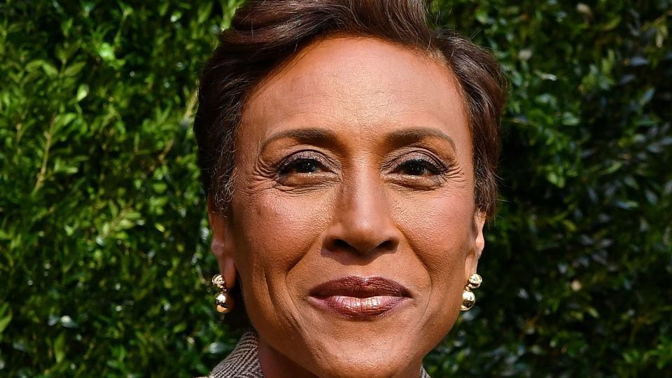 robin roberts smiles at the camera, she wears a brown suit jacket with a chevron pattern and a white blouse with gold jewelry