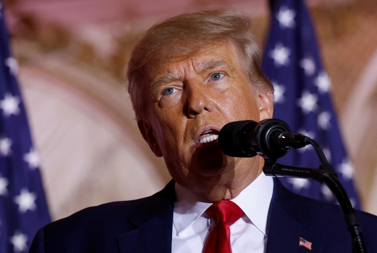 Donald Trump at the microphone, with two American flags behind him.