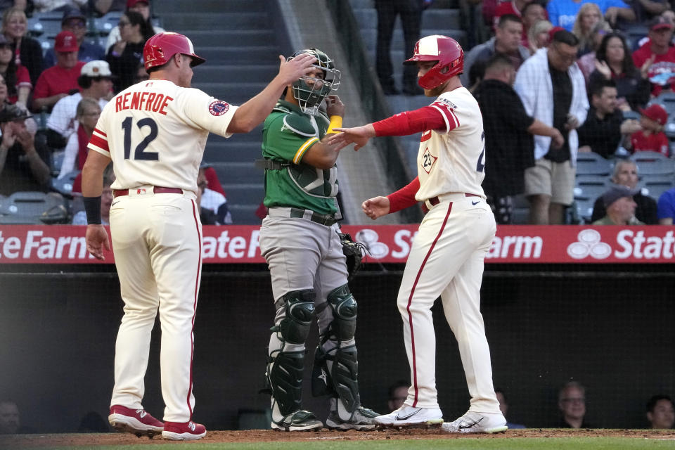 Los Angeles Angels' Hunter Renfroe, left, and Brandon Drury, right, congratulate each other after scoring on a ground rule double by Matt Thaiss as Oakland Athletics catcher Carlos Perez stands at the plate during the second inning of a baseball game Wednesday, April 26, 2023, in Anaheim, Calif. (AP Photo/Mark J. Terrill)