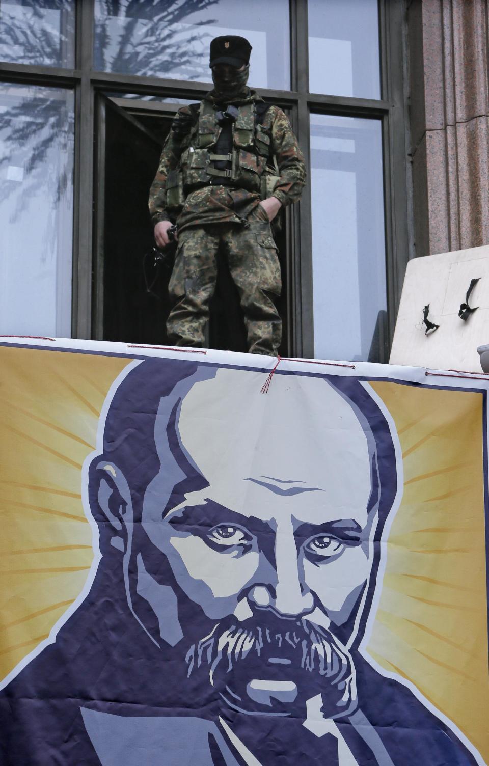 An opposition supporter stands above the portrait of a Ukrainian poet and national symbol Taras Shevchenko as he guards Kiev City Hall in Kiev, Ukraine, Sunday, Feb. 16, 2014. Anti-government demonstrators in Ukraine's capital ended their nearly three-month occupation of Kiev City Hall on Sunday as promised in exchange for the release of all jailed protesters. But tensions remained high as hundreds stayed outside the building, vowing to retake it if the government fails to drop all criminal charges against the protesters.(AP Photo/Efrem Lukatsky)