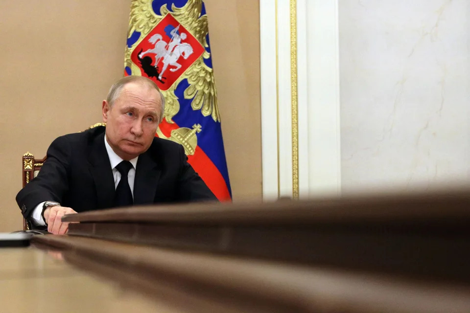 Russian President Vladimir Putin sitting at a table in front of a Russian flag.