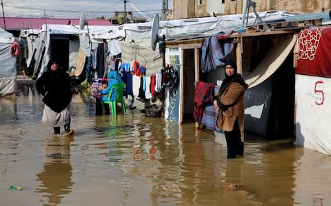 Syrian refugees stand in a pool of mud and rain water at a refugee camp, in the town of Bar Elias, in the Bekaa Valley, Lebanon - Credit: AP