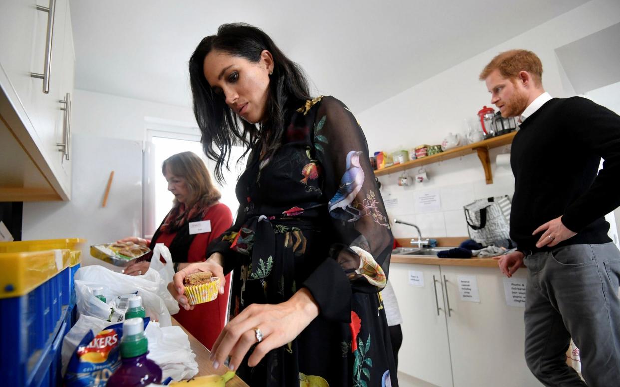 Prince Harry, behind, looks on as Meghan, Duchess of Sussex helps prepare food parcels during her visit to the One25 charity kitchen in Bristol - Pool reuters