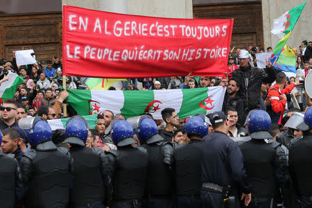 Police officers stand guard during a protest against the appointment of interim president, Abdelkader Bensalah and demanding radical changes to the political system in Algiers, Algeria April 10, 2019. The banner reads: "In Algeria, there are always people who write its history". REUTERS/Ramzi Boudina