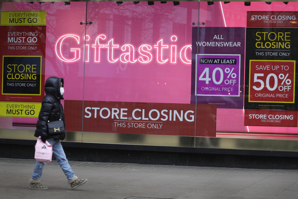 A woman walks past a Sale signs in the window of a closed shop on Oxford Street in London, Saturday, Dec. 26, 2020. London is currently in Tier 4 with all non essential retail shops closed and people have been asked to stay at home, on what is usually one of the busiest retail days of the year with the traditional Boxing Day sales in shops. (AP Photo/Kirsty Wigglesworth)