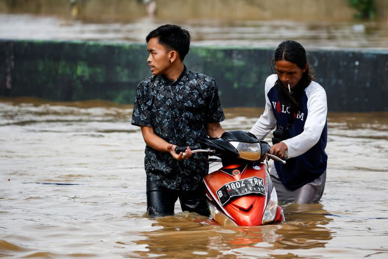 Men push a motorcycle through floodwaters at the Jatinegara area after heavy rains in Jakarta