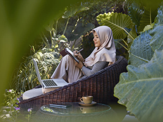 A woman on her laptop and writing on a pad