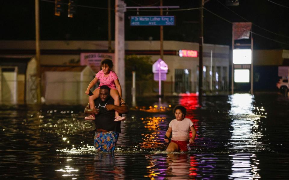 Jamir Lewis wades through floodwaters with his two daughters, Nylah and Aria, in Crystal River, Florida