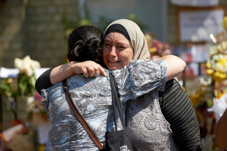 Women react after observing a minutes' silence in memory of the victims of the June 14 fire at the Grenfell Tower block, pictured on the horizon, in Kensington, west London, on June 19, 2017