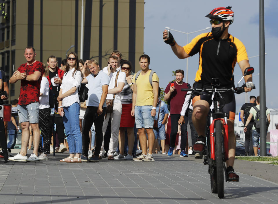 A man rides a bike and takes pictures as people queue to cast their votes in the Belarusian presidential election in Minsk, Belarus, Sunday, Aug. 9, 2020. Belarusians are voting on whether to grant incumbent president Alexander Lukashenko a sixth term in office, extending his 26-years rule, following a campaign marked by unusually strong demonstrations by opposition supporters. (AP Photo/Sergei Grits)