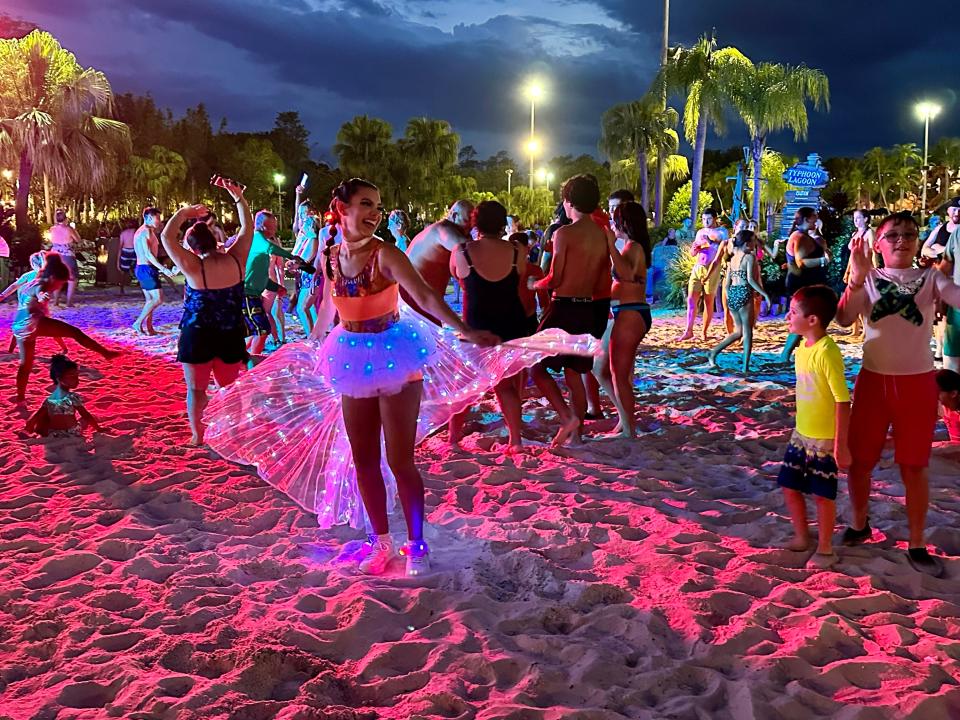 a pink and blue lit sandy area with groups of people dancing in light-up clothes