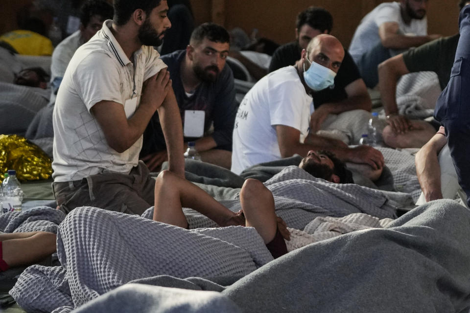 Survivors of a shipwreck rest in a warehouse at the port in Kalamata town, about 240 kilometers (150 miles) southwest of Athens, Wednesday, June 14, 2023. A fishing boat carrying migrants trying to reach Europe capsized and sank off Greece on Wednesday, authorities said, leaving at least 79 dead and many more missing in one of the worst disasters of its kind this year. (AP Photos/Thanassis Stavrakis)