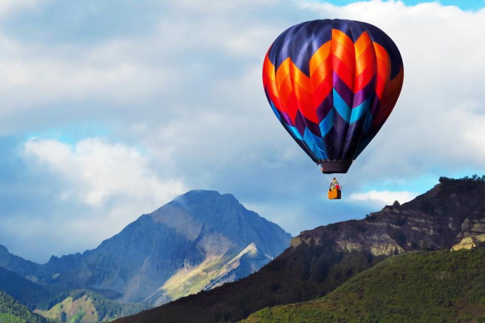 A vibrant hot air balloon hovers over the mountains near Aspen, Colorado