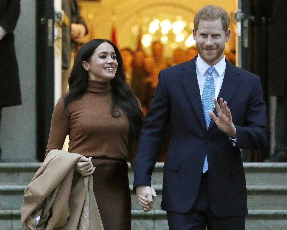 Meghan, Duchess of Sussex, and Prince Harry hold hands and walk out of a building.