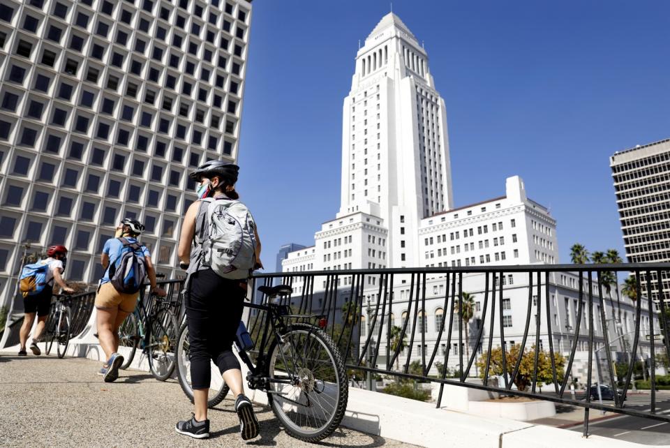 From left, Aimee Gilchrist, Marissa López, and Yvonne Condes, walk their bikes through downtown Los Angeles