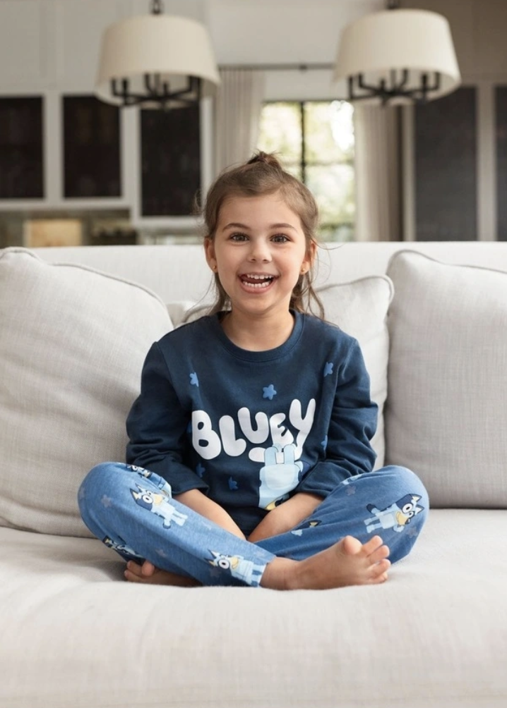 A young girl sitting smiling on the couch in Bluey themed pyjamas