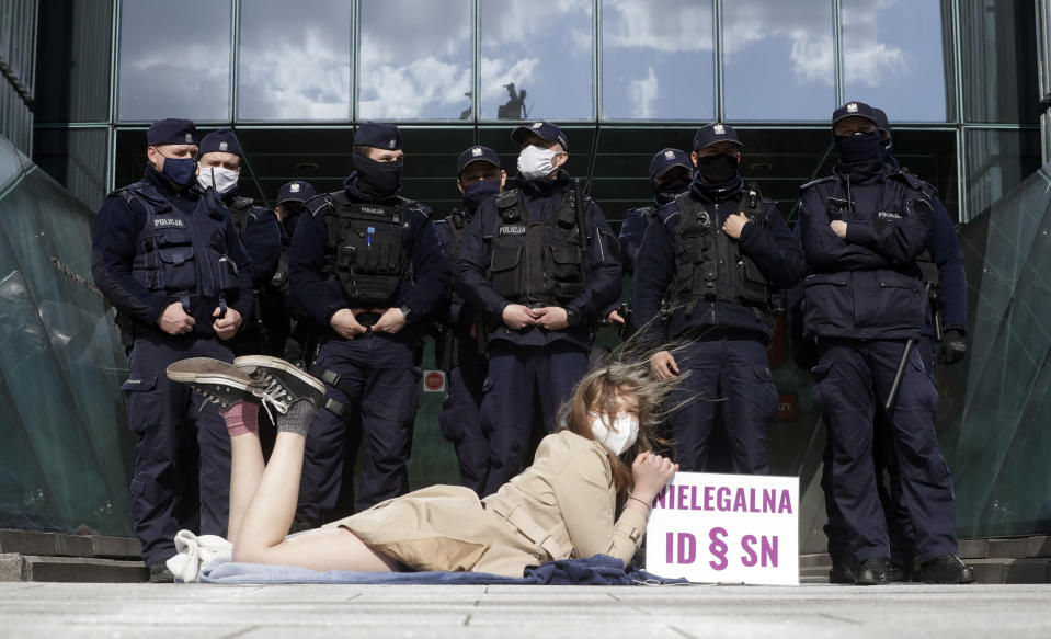 Policemen guard Poland's Supreme Court as a protester lies on the pavement in Warsaw, Poland, on Thursday, April 22, 2021. A disputed disciplinary body within Poland's Supreme Court is examining a motion that could result in the arrest of a judge who has become a symbol of the fight for an independent judiciary. The Disciplinary Chamber is due to decide whether to force Judge Igor Tuleya to answer to prosecutors about charges related to a ruling that went against the interests of the ruling Law and Justice party. Sign read in Polish "Illegal ID - SN”, where ID means Disciplinary Chamber and SN means Supreme Court. (AP Photo/Czarek Sokolowski)