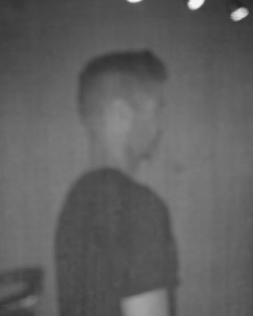 A black and white image of a man's profile, out of focus and through a window screen.