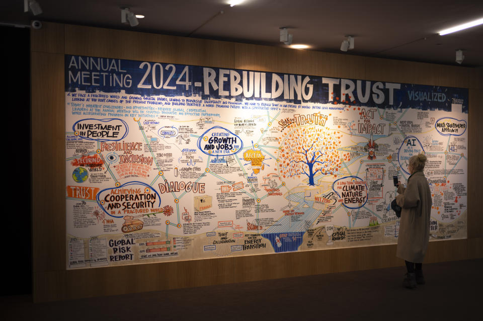 A woman takes photos of a wall featuring an artistic rendering of the main themes and ambitions discussed at the World Economic Forum's annual meeting under the theme of "Rebuilding Trust in Davos, Switzerland, Friday, Jan. 19, 2024. (AP Photo/Markus Schreiber)